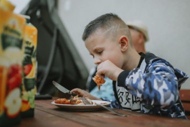 Young boy savoring a grilled chicken meal during an outdoor barbecue.